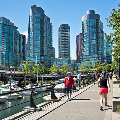 People walking along seawall in Coal Harbour neighbourhood of Vancouver, BC, Canada. City skyline with buildings and marina.